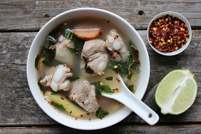 bowl of tom saap soup next to lime and bowl of pepper flakes